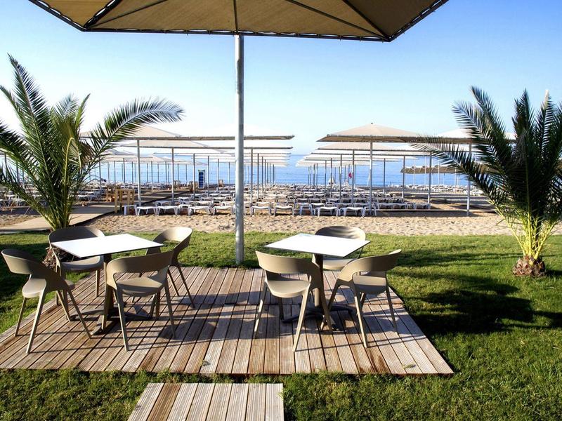 Dva stoly se židlemi pod slunečníky na terase s výhledem na moře.