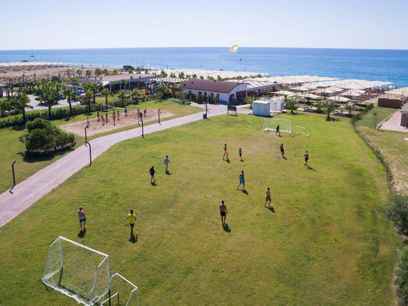 Skupina hraje fotbal na travnatém hřišti poblíž pláže a moře