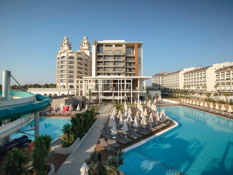 Velký hotel s bazénem, skluzavkou a slunečníky pod jasnou oblohou.