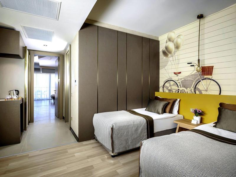 Moderní hotelový pokoj se dvěma jednolůžky, skříňovou stěnou a dekorací kola na stěně.