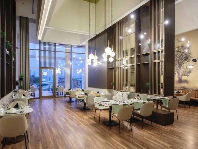 Moderní restaurace s dřevěnou podlahou a velkými okny, elegantní posezení u stolů a židlí.