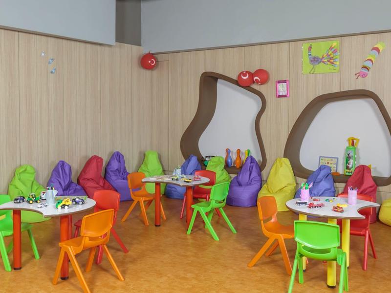 Barevná herna pro děti s malými stoly, židlemi, sedacími pytli a nástěnnými zrcadly.