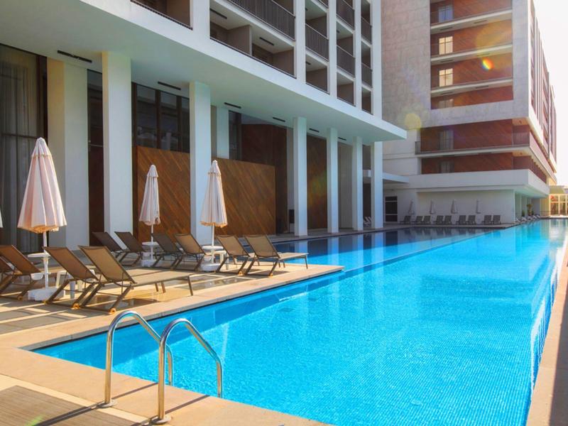 Moderní venkovní bazén s lehátky a slunečníky vedle hotelové budovy při západu slunce.