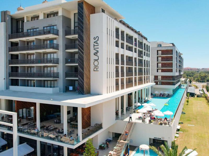 Moderní hotel s velkým bazénem a venkovní terasou pod jasnou oblohou.