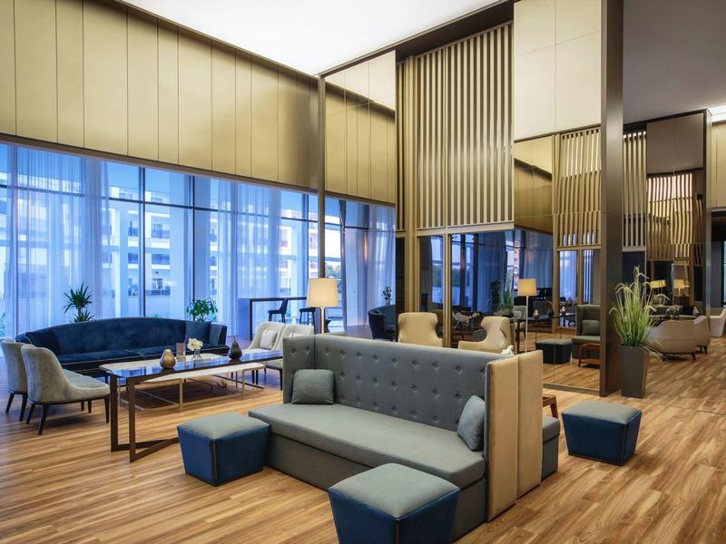 Moderní hotelová lobby s velkými okny, útulnými posezeními a dřevěnou podlahou.