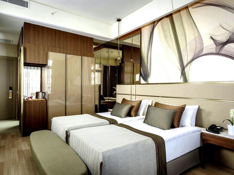 Moderní hotelový pokoj se dvěma samostatnými postelemi, dřevěným nábytkem a abstraktní výzdobou stěn.