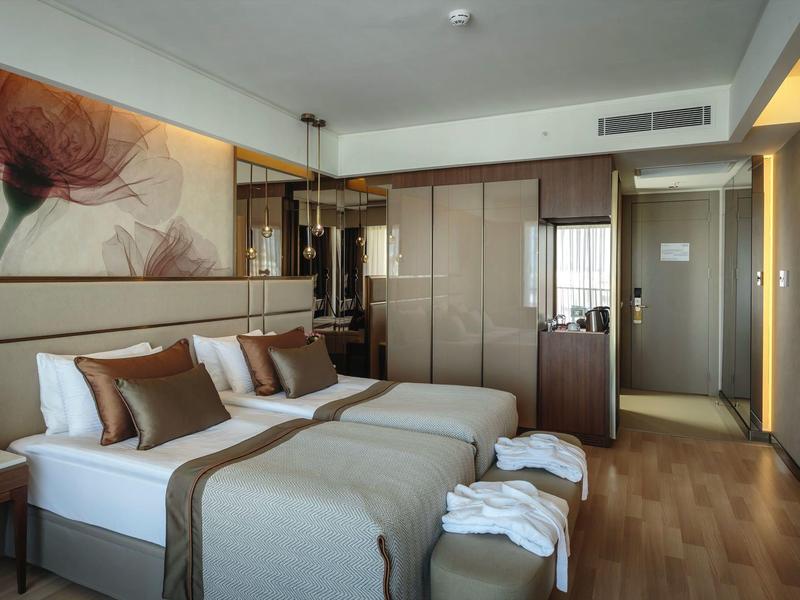 Moderní hotelový pokoj se dvěma jednolůžky, jednoduchým dřevěným nábytkem a dekorativním nástěnným uměním.