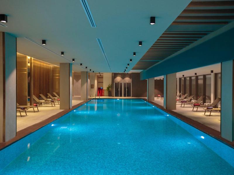 Vnitřní bazén s lehátky a moderním stropním osvětlením v hotelu