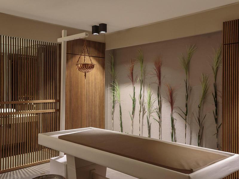 Moderní spa pokoj s masážním stolem, dřevěným obložením a dekorací ze stěnových rostlin.