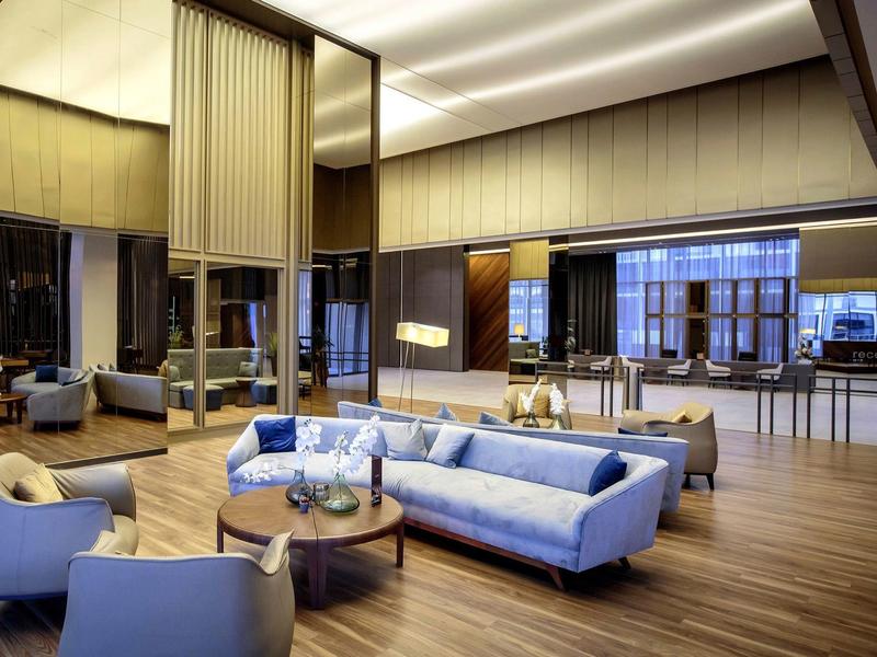 Prostorná hotelová hala s modrými pohovkami, dřevěnou podlahou a velkými okny.