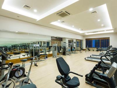 Großer heller Fitnessraum mit verschiedenen Trainingsgeräten und Spiegelwand.