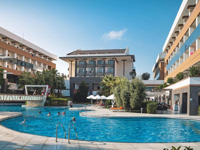 Großer runder Pool mit Menschen, umgeben von modernen, mehrstöckigen Hotelgebäuden unter blauem Himmel.