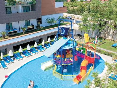 Schwimmbad mit buntem Wasserspielplatz, Rutschen und weißen Sonnenschirmen neben Liegestühlen.