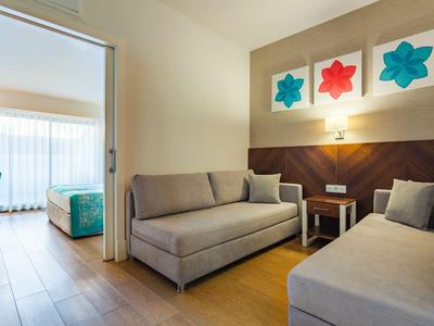 Modernes Hotelzimmer mit zwei Sofas, Wandkunst und angrenzendem Schlafzimmer mit großem Fenster.