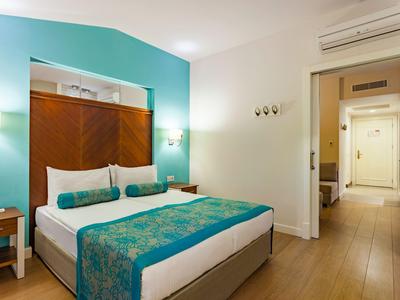 Modernes Hotelzimmer mit Doppelbett, türkisfarbenen Akzenten und hellen Holzmöbeln.