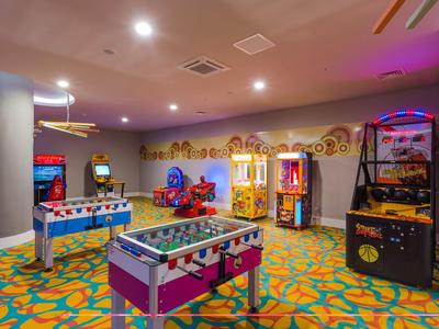 Bunte Spielhalle mit Kicker, Flipperautomaten und farbenfrohem Teppichmuster einer Freizeitecke.