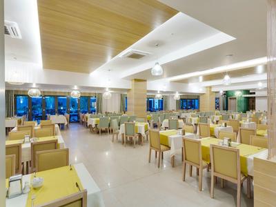 Großer, heller Speisesaal mit gelben Stühlen, Holztischen und modernen Deckenleuchten.