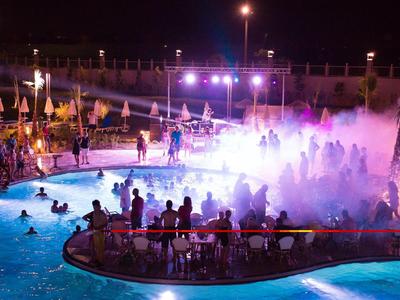 Beleuchteter Pool bei Nacht mit Menschen, Nebel und bunter Bühnenbeleuchtung.