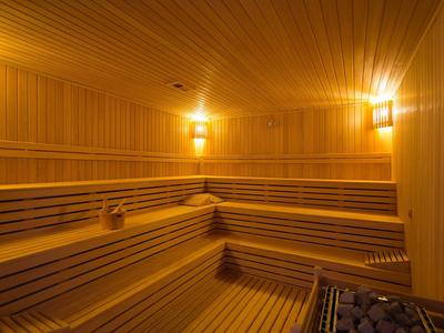 Helle hölzerne Sauna mit mehrstufigen Bänken und warmen Wandlampen.