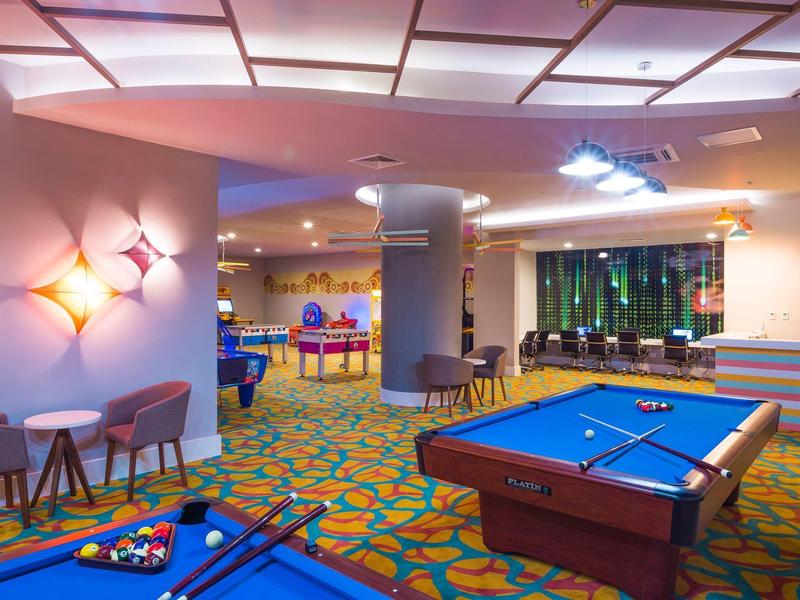 Světle osvětlená herna hotelu s kulečníkovými stoly a pohodlným posezením.