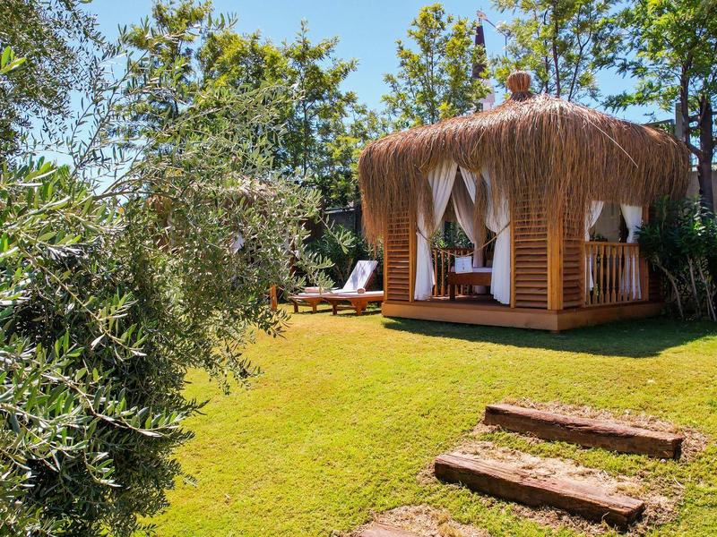 Plátěný altán s závěsy na zelené trávě obklopený stromy a kamennými schody.