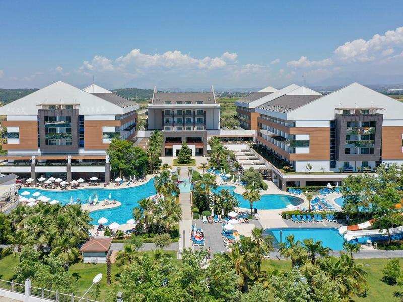 Velký hotelový komplex s bazénem, palmami a moderními budovami pod modrou oblohou.