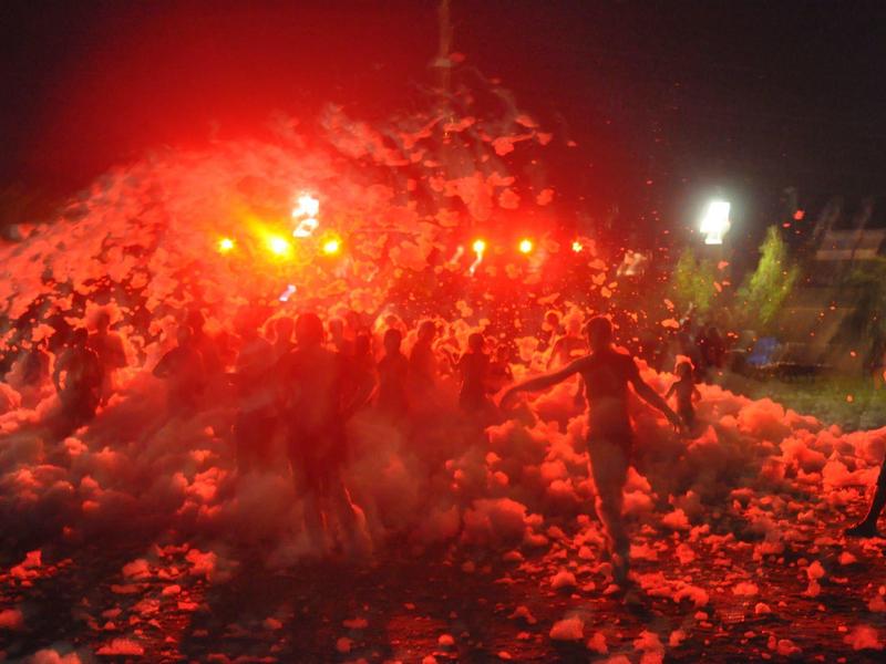 Lidé na noční párty s pěnou a silným červeným osvětlením.