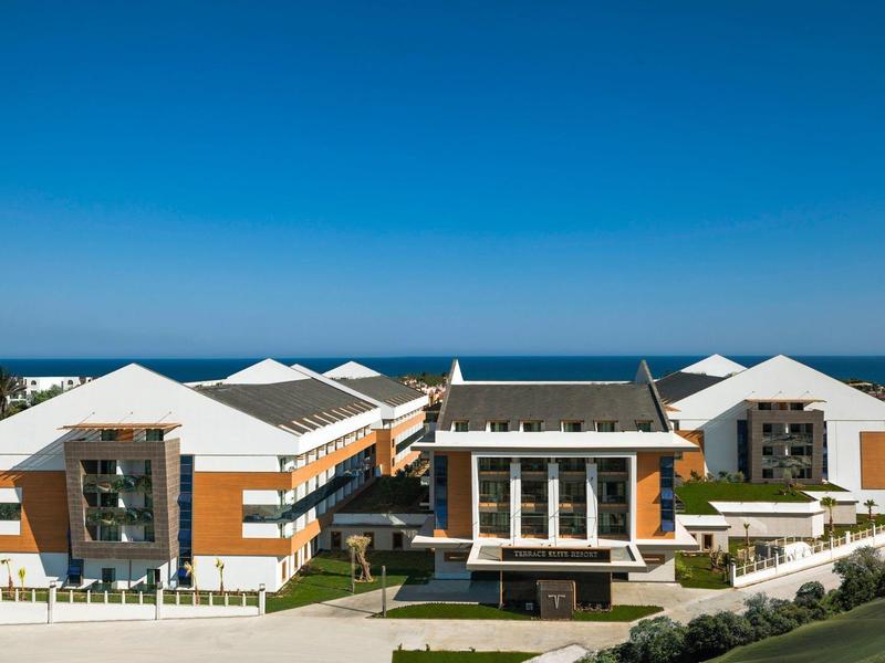 Moderní hotel s bílými střechami a výhledem na moře pod jasnou modrou oblohou.