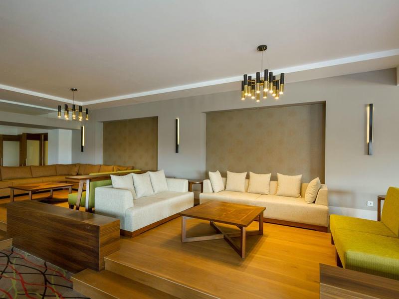 Moderní hotelový salon s bílými a žlutými pohovkami, dřevěnými stolky, elegantním osvětlením.