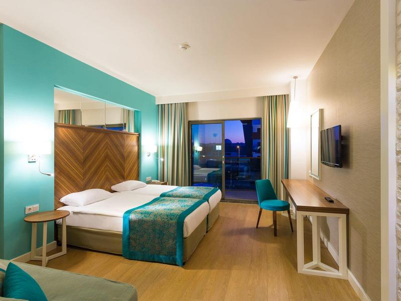 Moderní hotelový pokoj s manželskou postelí, psacím stolem, židlí a nočním výhledem z okna.