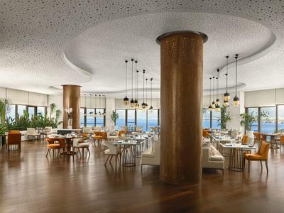 Helles, modernes Restaurant mit Rundsäulen, Holzboden und großen Fenstern mit Meerblick.