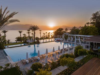Hotelpool mit Liegestühlen und Palmen bei Sonnenuntergang, Blick auf das Meer.