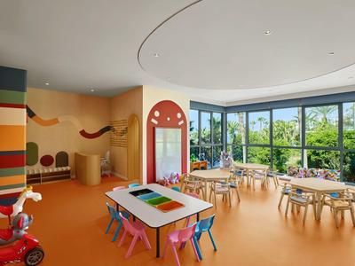 Ein heller, bunter Kinderspielraum mit Tischen, Stühlen und großen Fenstern in einem Hotel.