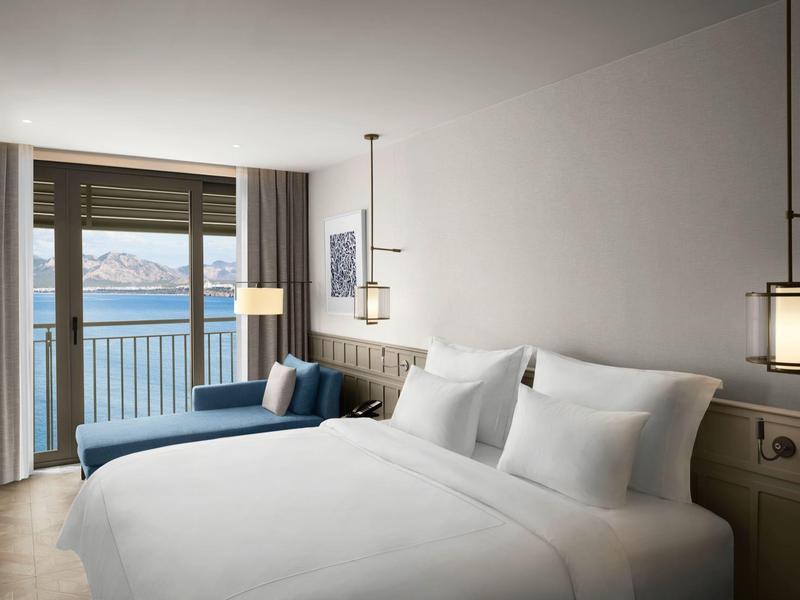 Moderní hotelový pokoj s velkou postelí, posezením a balkonem s výhledem na moře.