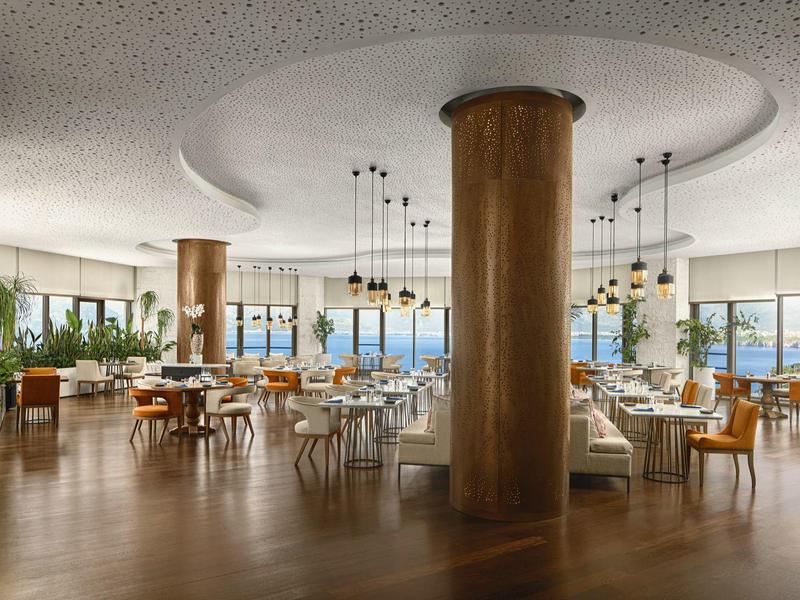 Moderní, světlá hotelová jídelna s velkými dřevěnými sloupy a panoramatickými okny.