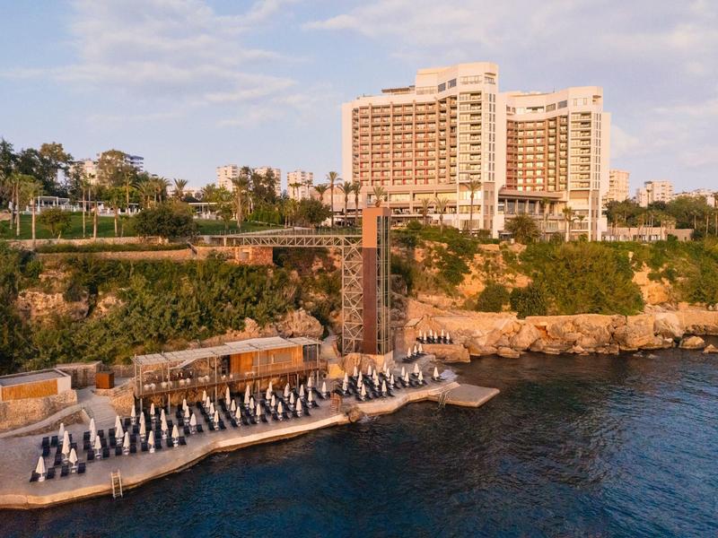 Hotel na pobřeží s terasou a lehátky u vody pod jasnou oblohou.