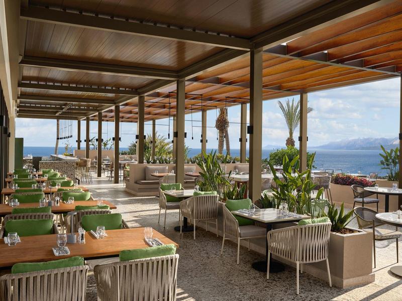 Hotelová terasa s posezením a výhledem na moře pod dřevěným přístřeškem.