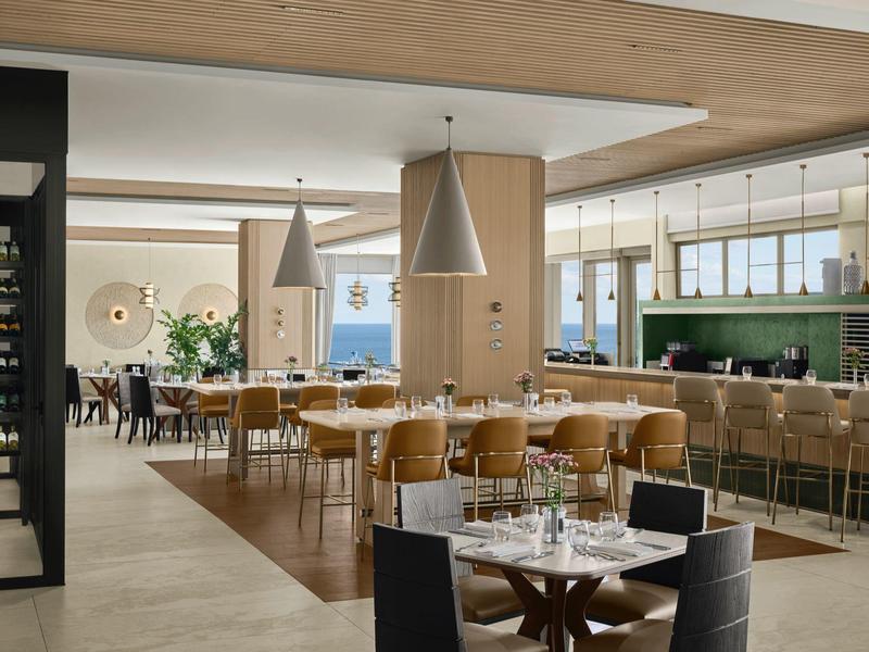 Moderní hotelová jídelna s dřevěnými židlemi, velkými okny a útulným osvětlením.