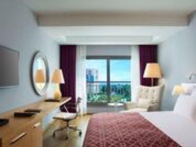 Habitación de hotel moderna con cama, escritorio, lámparas y vista al mar desde el balcón.