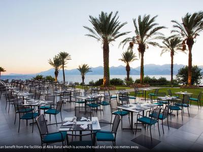 Terraza al aire libre con mesas y sillas junto a palmeras frente al mar durante el atardecer.