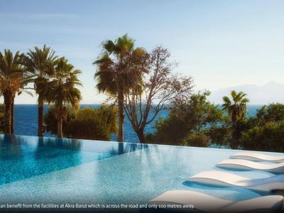 Infinity pool with loungers surrounded by palm trees and sea view under clear sky.