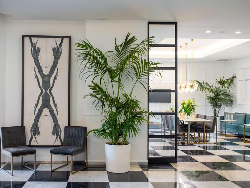 Lobby de hotel moderna con suelo de ajedrez en blanco y negro, plantas y área de descanso.