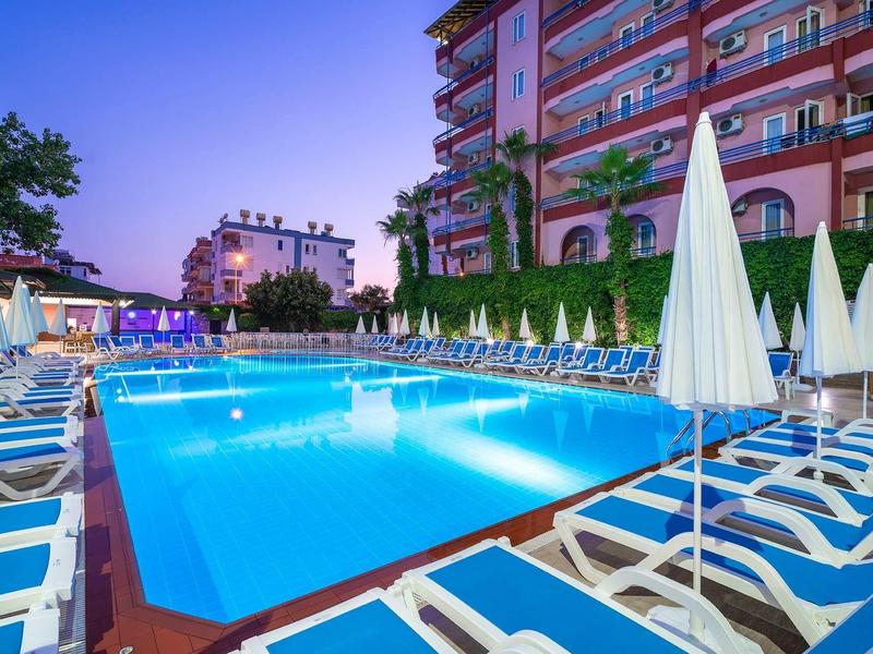 Piscine extérieure avec chaises longues et parasols, entourée d'un hôtel moderne au crépuscule.