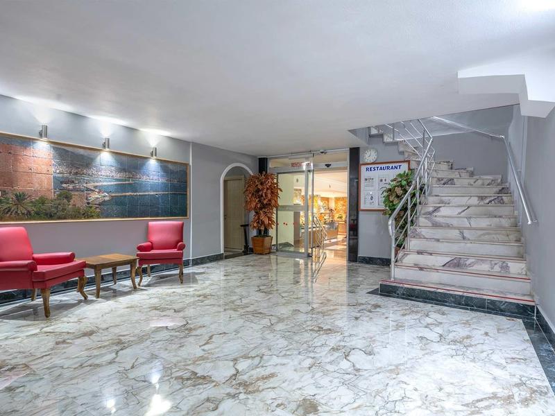 Hall d'hôtel avec fauteuils rouges, sol en marbre et escalier en pierre.