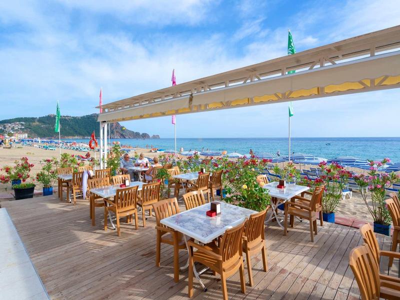 Terrasse de restaurant en bois avec vue sur la plage et la mer sous un ciel clair.
