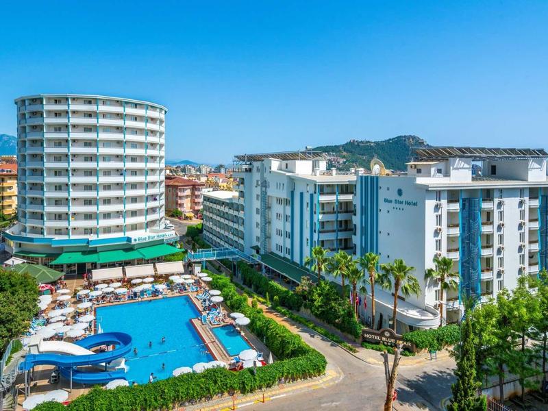 Complexe hôtelier moderne avec piscine extérieure, bâtiments blancs et paysage urbain en arrière-plan.