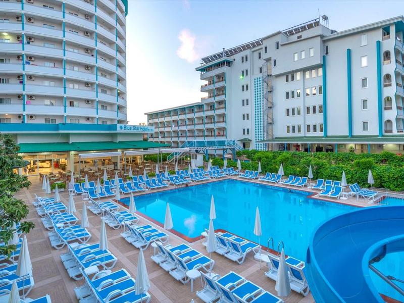 Piscine extérieure avec chaise longue bleue près d'un hôtel moderne et des arbustes.