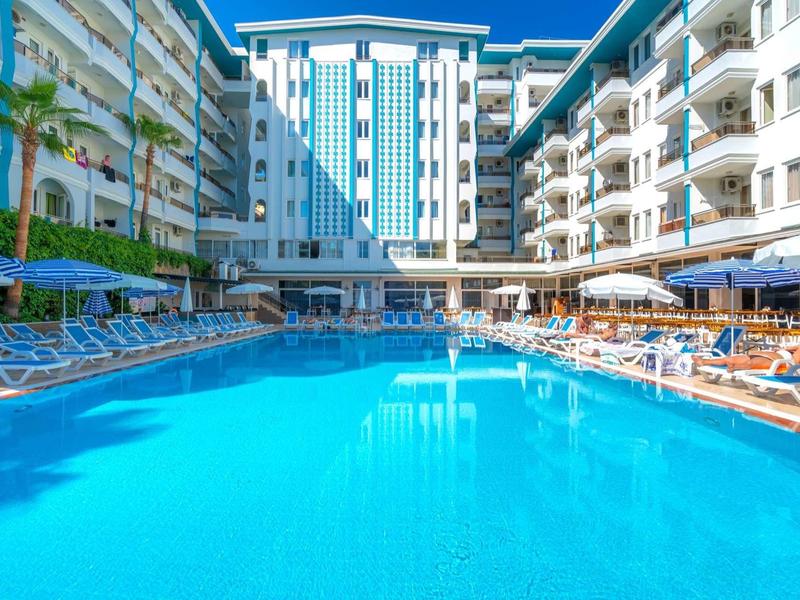 Grande piscine bleue entourée de chaises longues près d'un hôtel moderne à plusieurs étages.