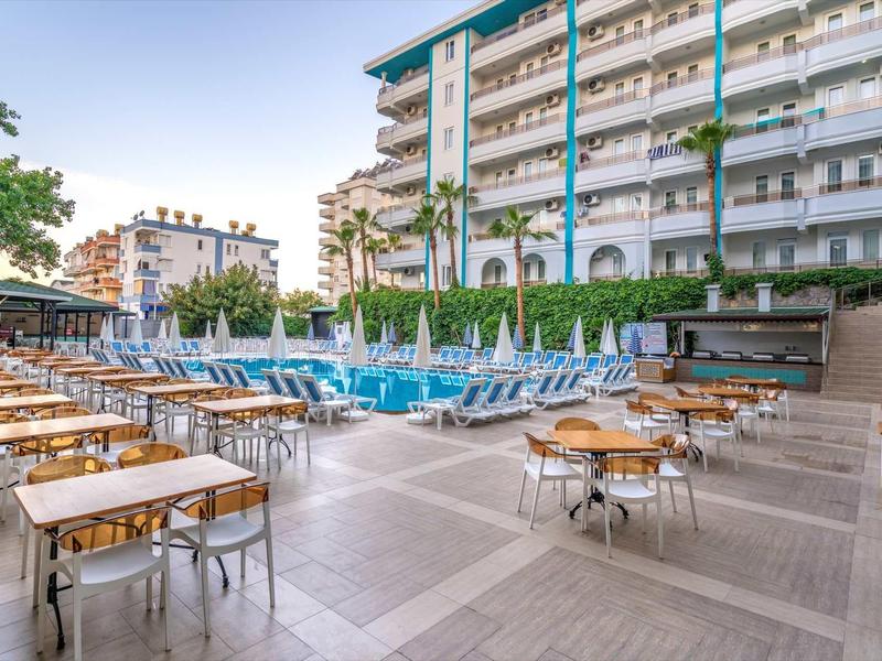 Terrasse extérieure avec tables et chaises près d'une piscine entourée d'un immeuble.