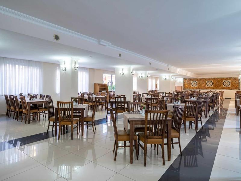 Salle à manger spacieuse avec tables et chaises en bois, éclairage moderne et sol carrelé.
